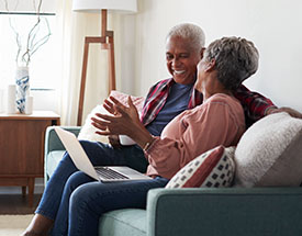 An older couple sitting on the couch talking with a computer on their laps