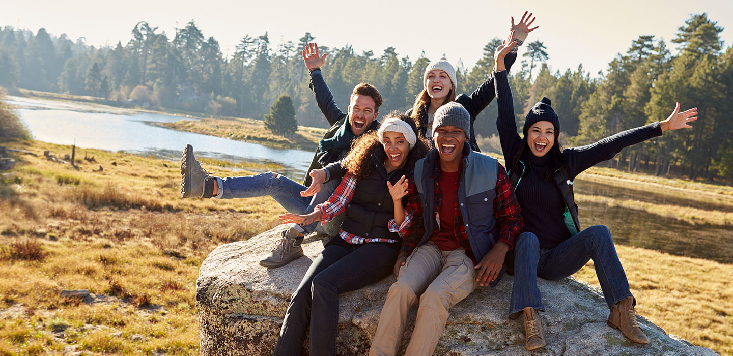 Group of friends smiling and laughing while sitting on a large rock outdoors