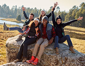 Group of friends smiling and laughing while sitting on a large rock outdoors