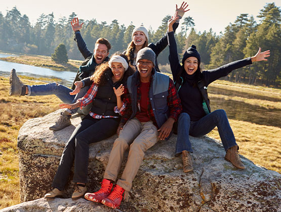 Group of friends smiling and laughing while sitting on a large rock outdoors