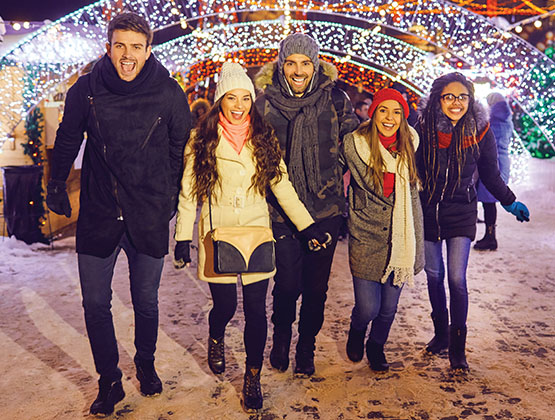 Image of friends smiling and walking among holiday lights