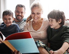 A family of four sitting on a couch and reading a book