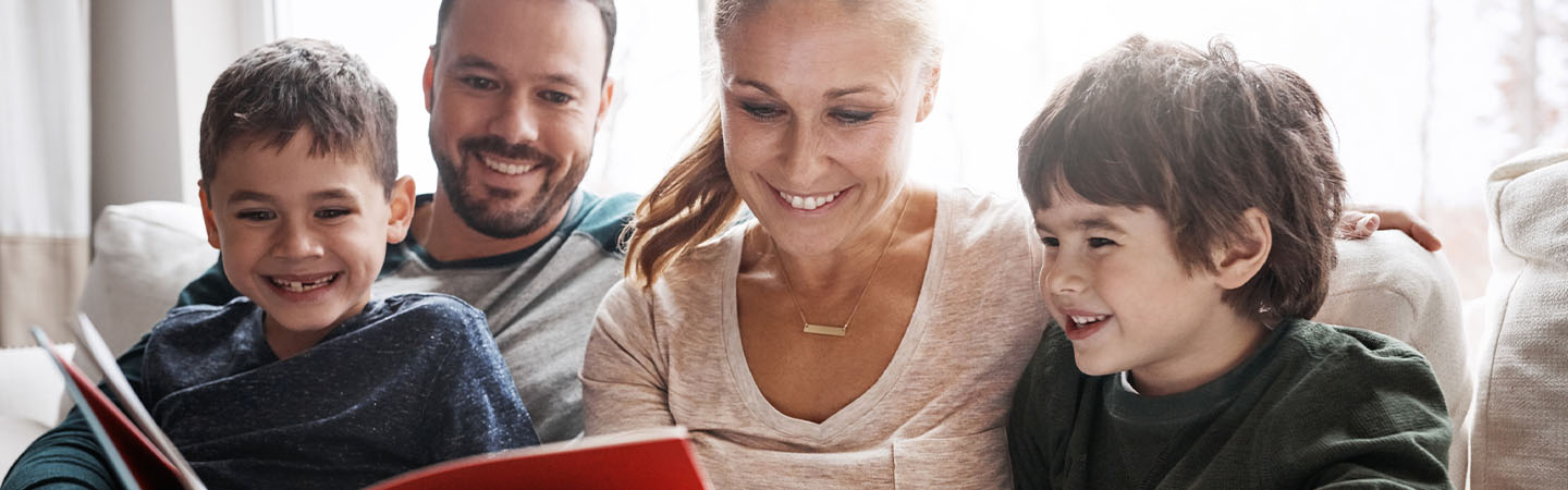 A family of four reading a book on a couch