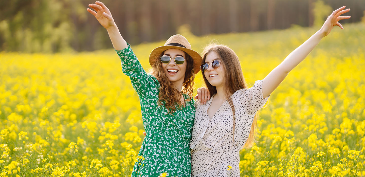 Two joyful women standing in a field of yellow flowers