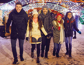 Image of friends smiling and walking among holiday lights