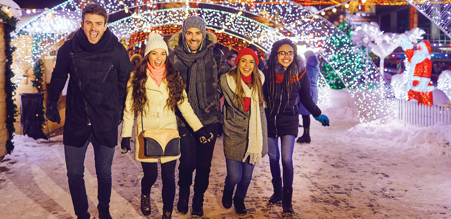 Image of friends smiling and walking among holiday lights